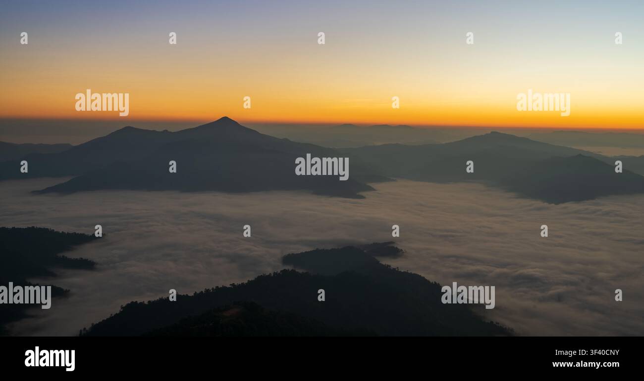 Bellissimo cielo all'alba con toni caldi sopra montagne nebbiose e un cielo ampio e aperto. Foto Stock