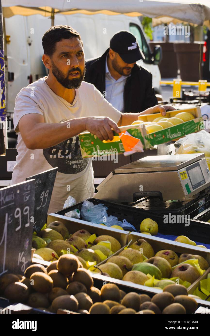 Un venditore di frutta che posa una scatola di prodotti freschi su una bilancia in un mercato all'aperto ad Arles, Francia. Foto Stock