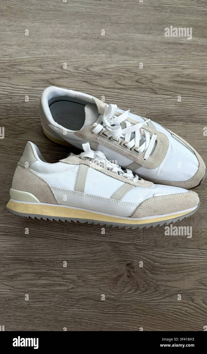 Scarpe da ginnastica bianche e beige con tessuto strutturato e suole in gomma posizionate su un pavimento di legno Foto Stock