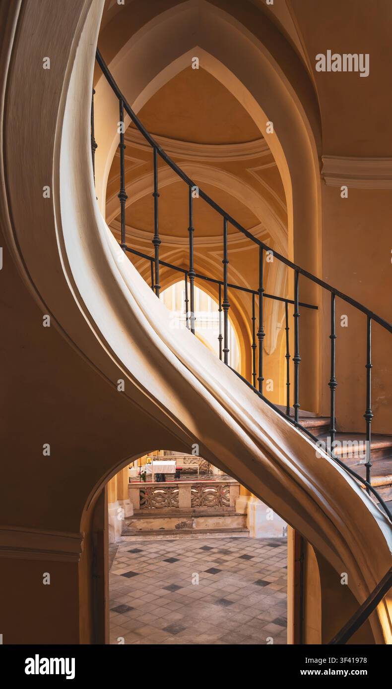 Una scala a chiocciola si snoda verso l'alto in un edificio storico. Le pareti presentano un design semplice. La luce del sole filtra da una finestra vicino alla cima. I passi riecheggiano nello spazio silenzioso. Foto Stock