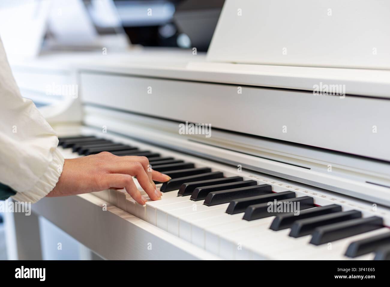 Primo piano di una mano che suona un pianoforte digitale bianco. La mano di una persona suona i tasti neri e bianchi di un pianoforte digitale bianco in un ambiente interno luminoso Foto Stock