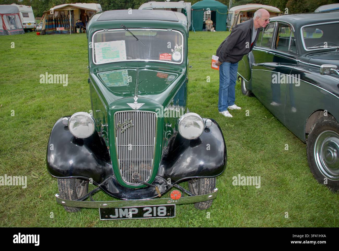 Classica berlina vintage britannica Austin 7 parcheggiata sull'erba con uno spettatore che ispeziona un veicolo adiacente a una mostra di auto d'epoca. Foto Stock