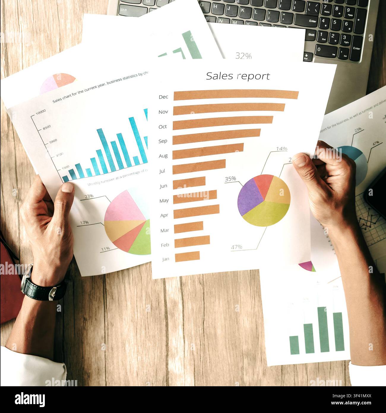 Una persona tiene rapporti di vendita con grafici colorati su una scrivania di legno. Le mani mostrano attenzione all'analisi dei dati. Ideale per progetti di business, finanza o marketing Foto Stock
