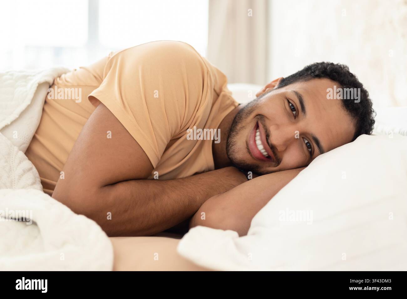Giovane uomo sorridente sdraiato a letto, rilassato e comodo a casa, concetto di sonno Foto Stock