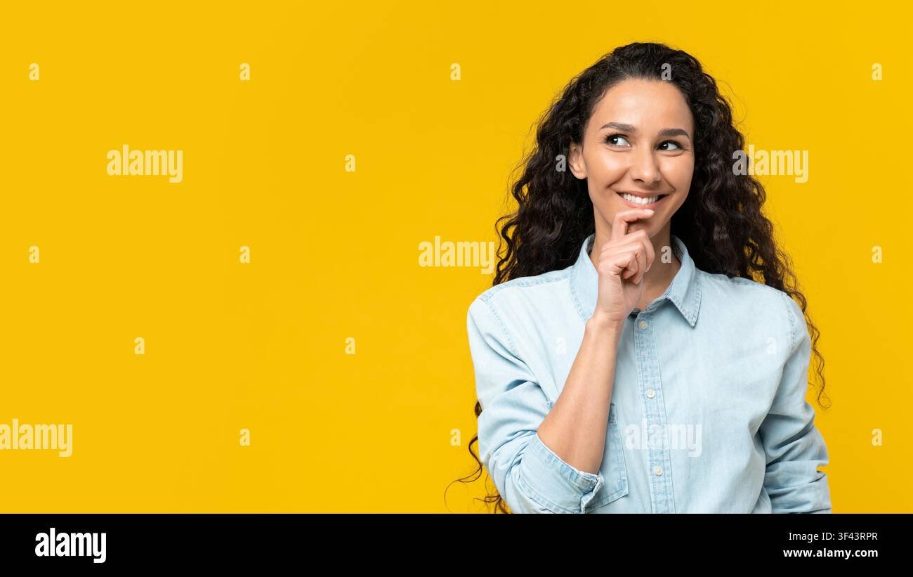 Giovane donna pensierosa con capelli ricci che sorride e guarda verso l'alto, sfondo giallo Foto Stock