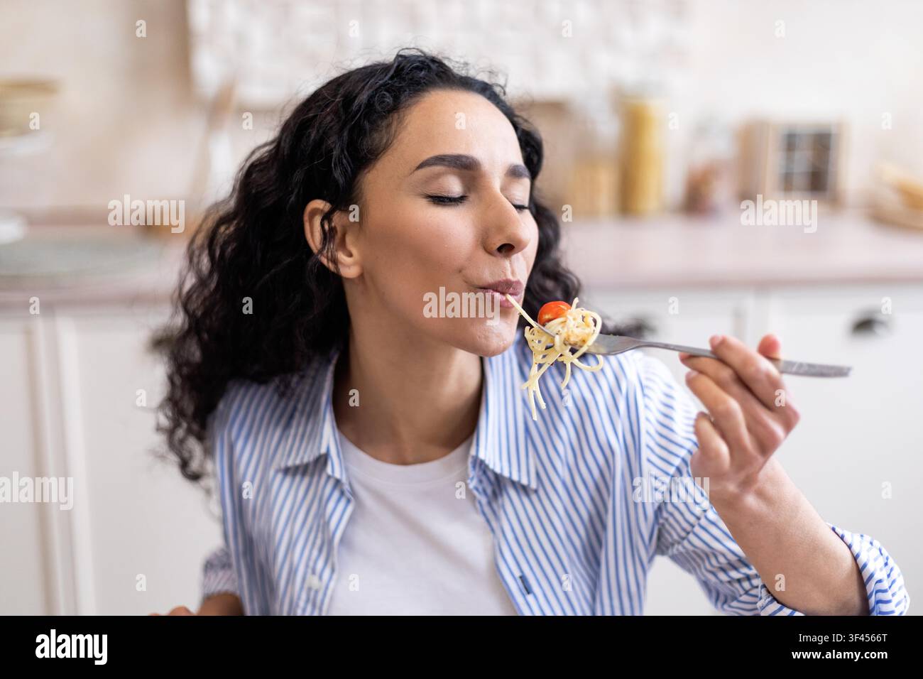 Donna felice che assapora un piatto di pasta in cucina, abbracciando l'esperienza culinaria Foto Stock
