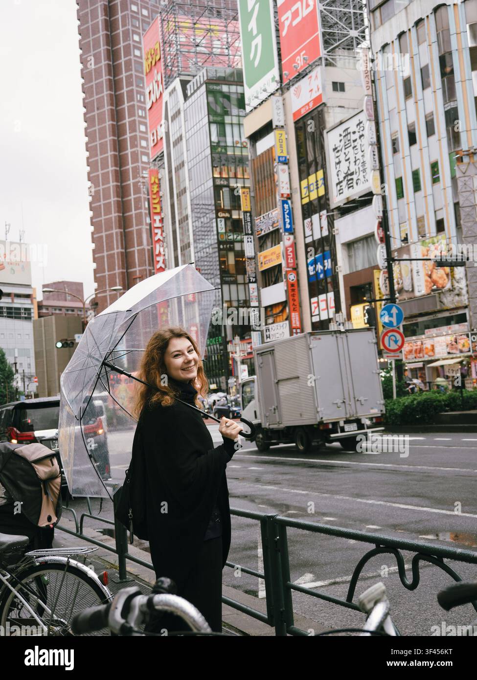 Giovane donna che tiene un ombrello trasparente su una strada con cartelloni pubblicitari in una giornata di pioggia a Shinjuku, Tokyo, Giappone Foto Stock
