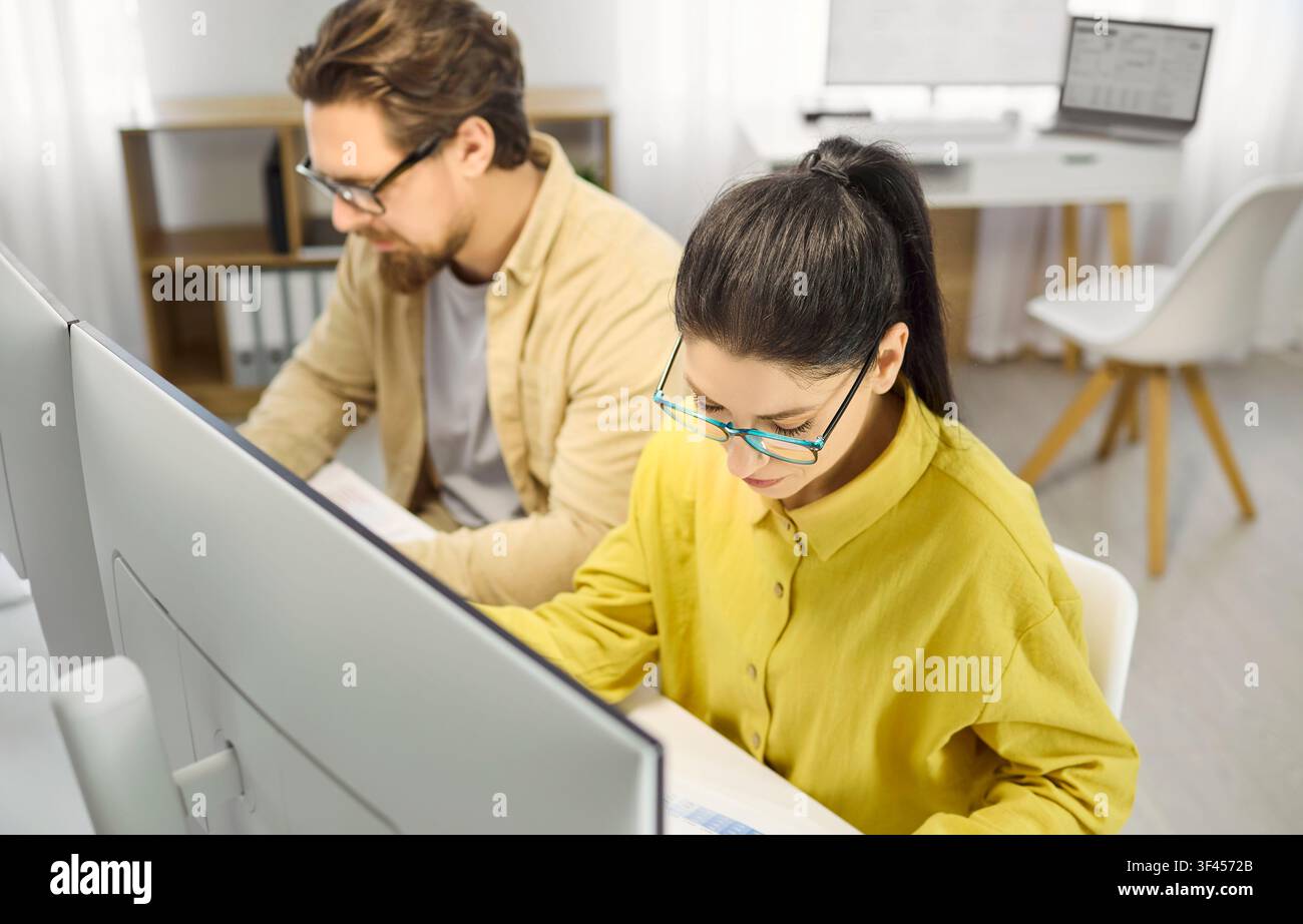 Analista femminile concentrata che lavora su fogli di calcolo ai monitor da tavolo in ufficio Foto Stock