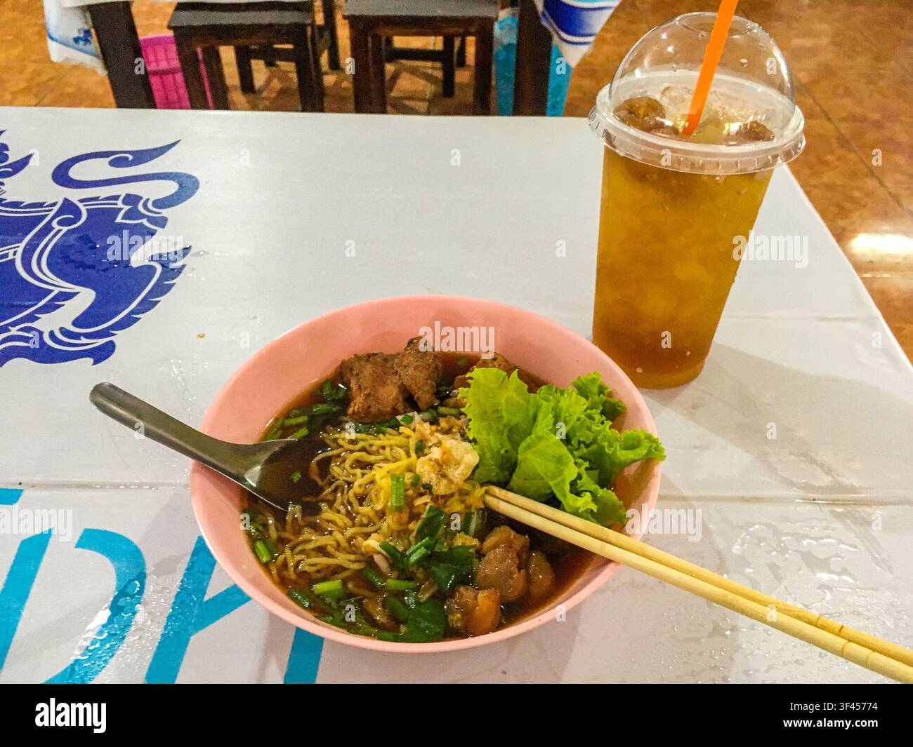Una ciotola di zuppa di noodle alle uova saporita servita con maiale tenero e lattuga fresca, accompagnata da una rinfrescante bevanda al longan ghiacciata, gustata in una trattoria locale Foto Stock