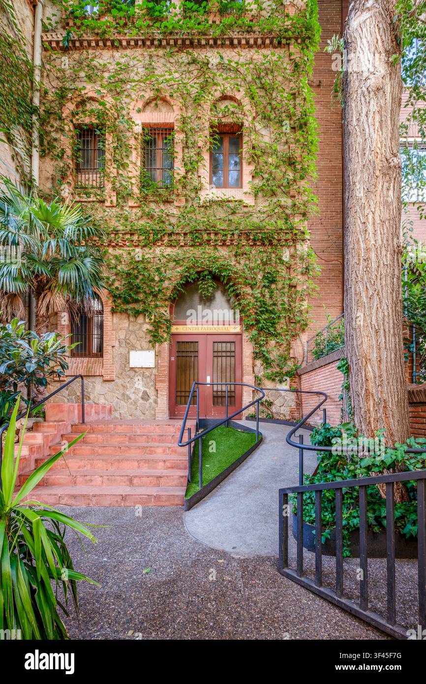 Barcellona – Spagna – 14 luglio 2026: Ingresso dell'edificio con scale in pietra, rampa per disabili, edera rampicante, facciata in pietra, porte rosse, architettura urbana Foto Stock