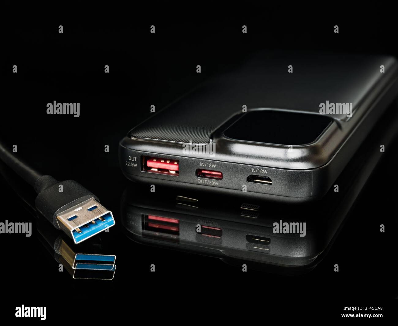 Power bank portatile nera con display digitale al 100 percento, riflessione e cavo USB Type-A su superficie nera. Pacco batteria esterno moderno per dispositivi mobili Foto Stock