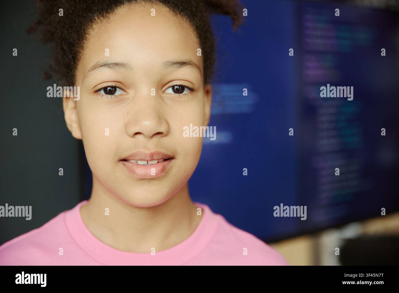 Ritratto di una ragazza adolescente nera che guarda verso la telecamera con uno schermo di codifica sullo sfondo, che rappresenta l'apprendimento digitale e le competenze tecnologiche dei giovani. Utile per l'istruzione STEM, corsi di programmazione, outreach tecnologico Foto Stock