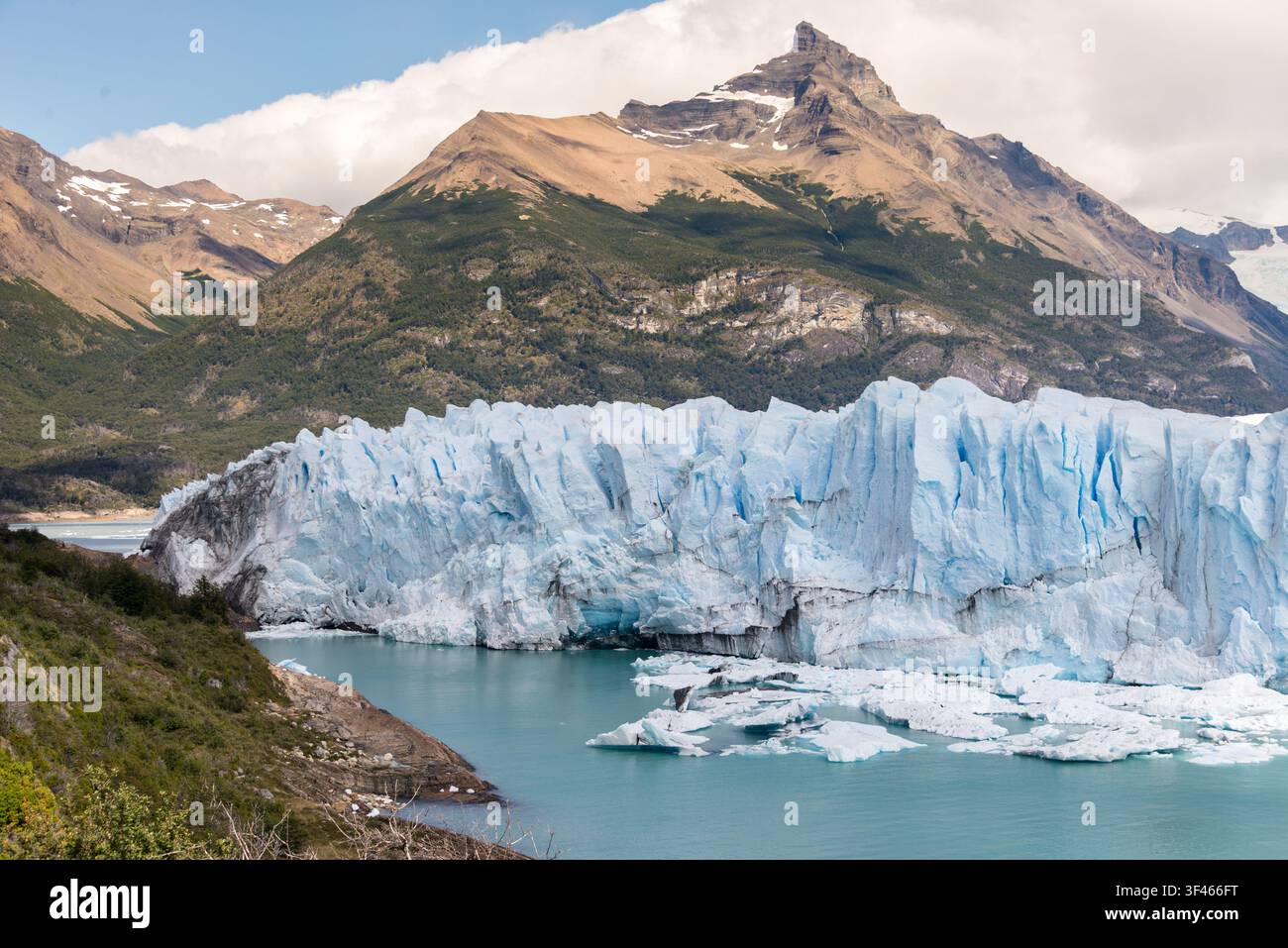 Ghiacciaio massiccio in un lago turchese con montagne impervie sotto un cielo blu Foto Stock