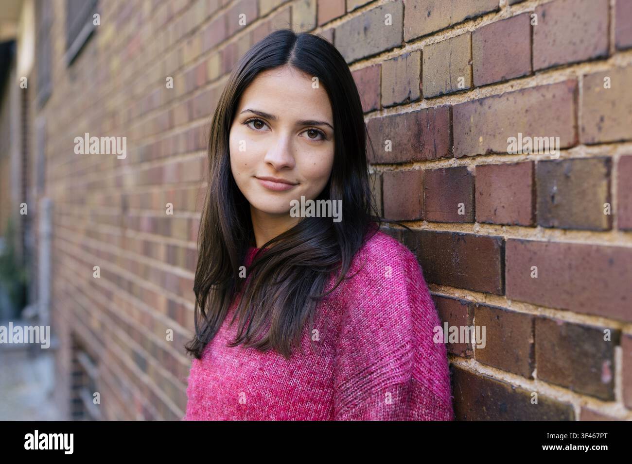 Giovane donna in maglione rosa si appoggia a un muro di mattoni Foto Stock