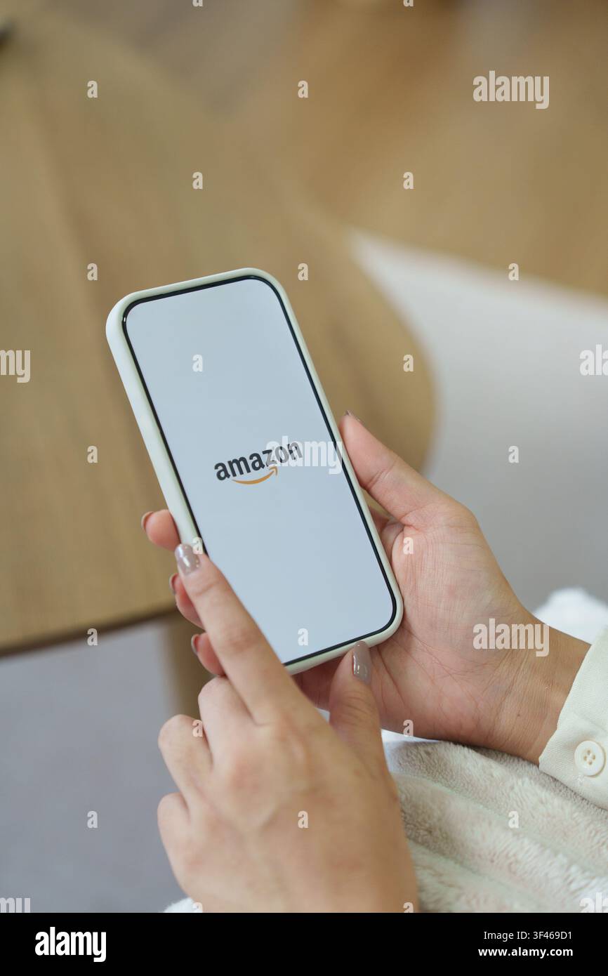 Amazon logo su una schermata dello smartphone in una stanza buia e un dito puntato a. Foto Stock