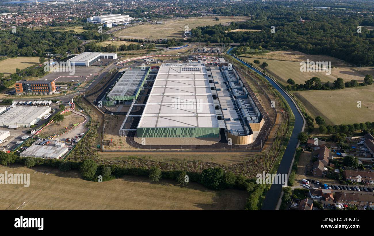 Vista aerea di un grande centro dati moderno con pannelli solari sul tetto, circondato da campi verdi, un canale e abitazioni suburbane a Waltham Foto Stock