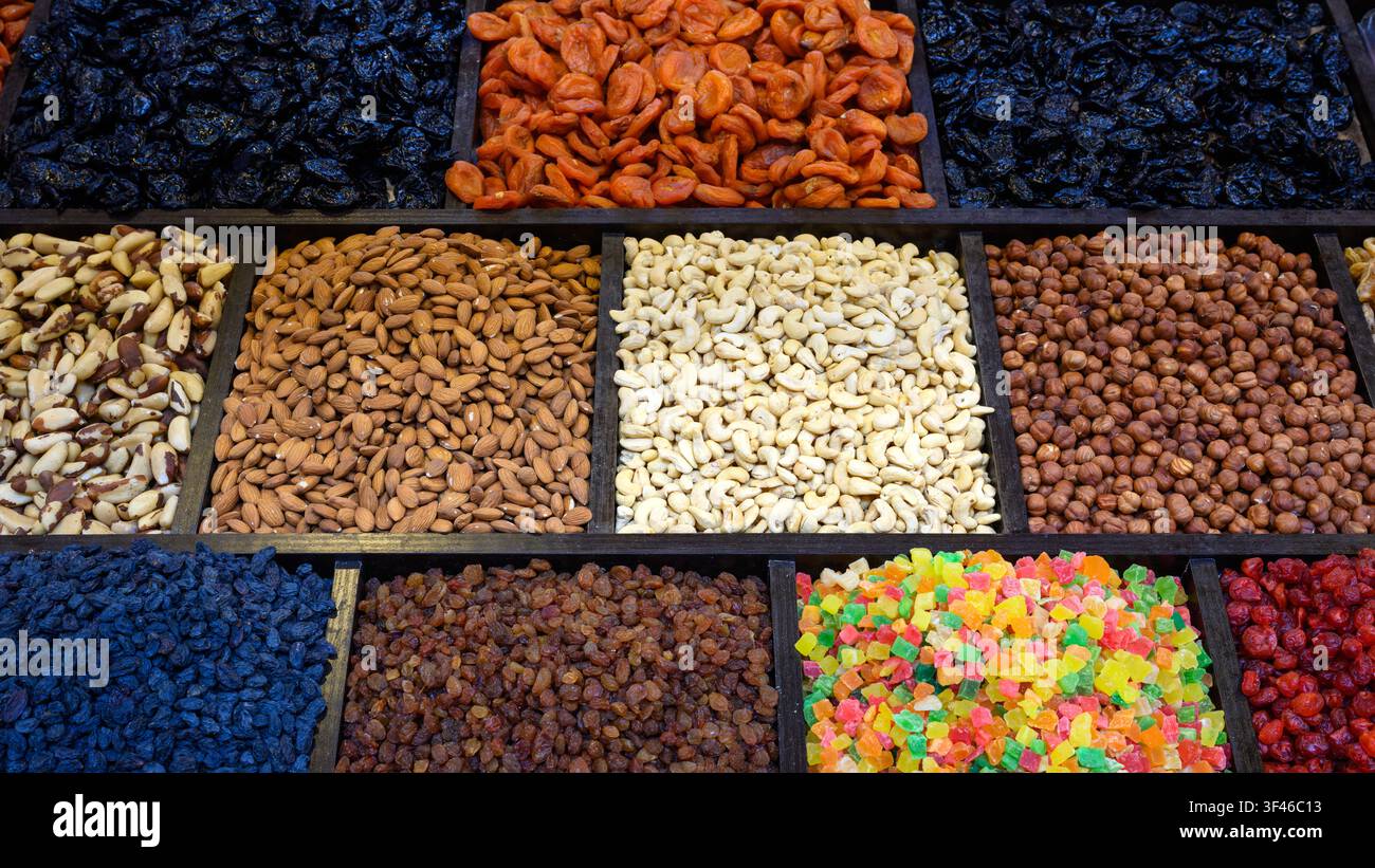Una fotografia aerea che mostra una varietà colorata di noci e frutta secca disposta in un vassoio di legno compartimentato. La fila superiore contiene Foto Stock