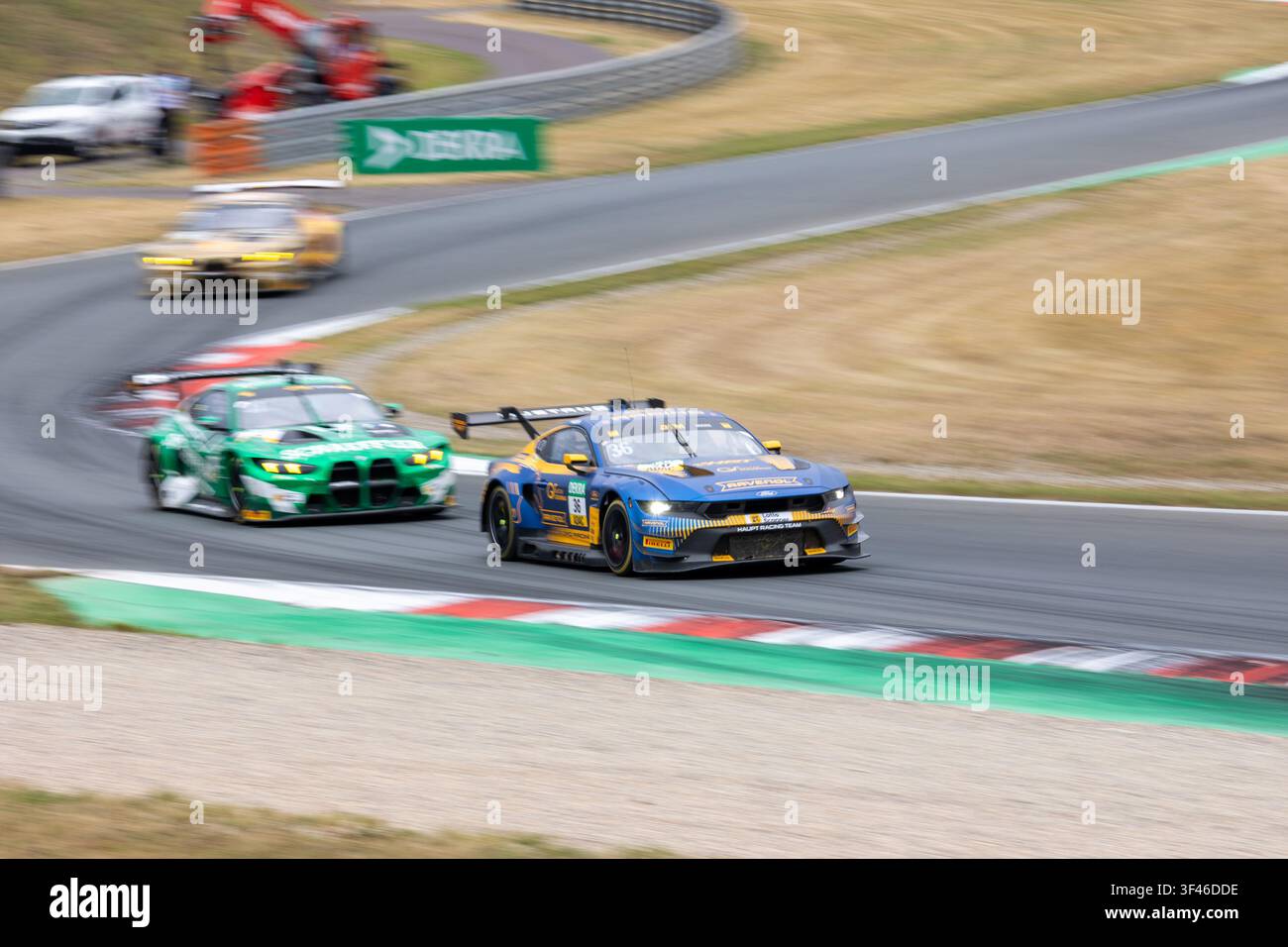 Oschersleben, Germania. 26 luglio 2026. Arjun Maini guida Marco Wittmann attraverso la curva veloce di Oschersleben con la sua auto blu e gialla numero 36 HRT Ford Mustang GT3. La vettura verde numero 11 Schubert BMW M4 GT3 Evo segue da vicino mentre il sfocato per movimento sottolinea la velocità della DTM 2026. Foto Stock