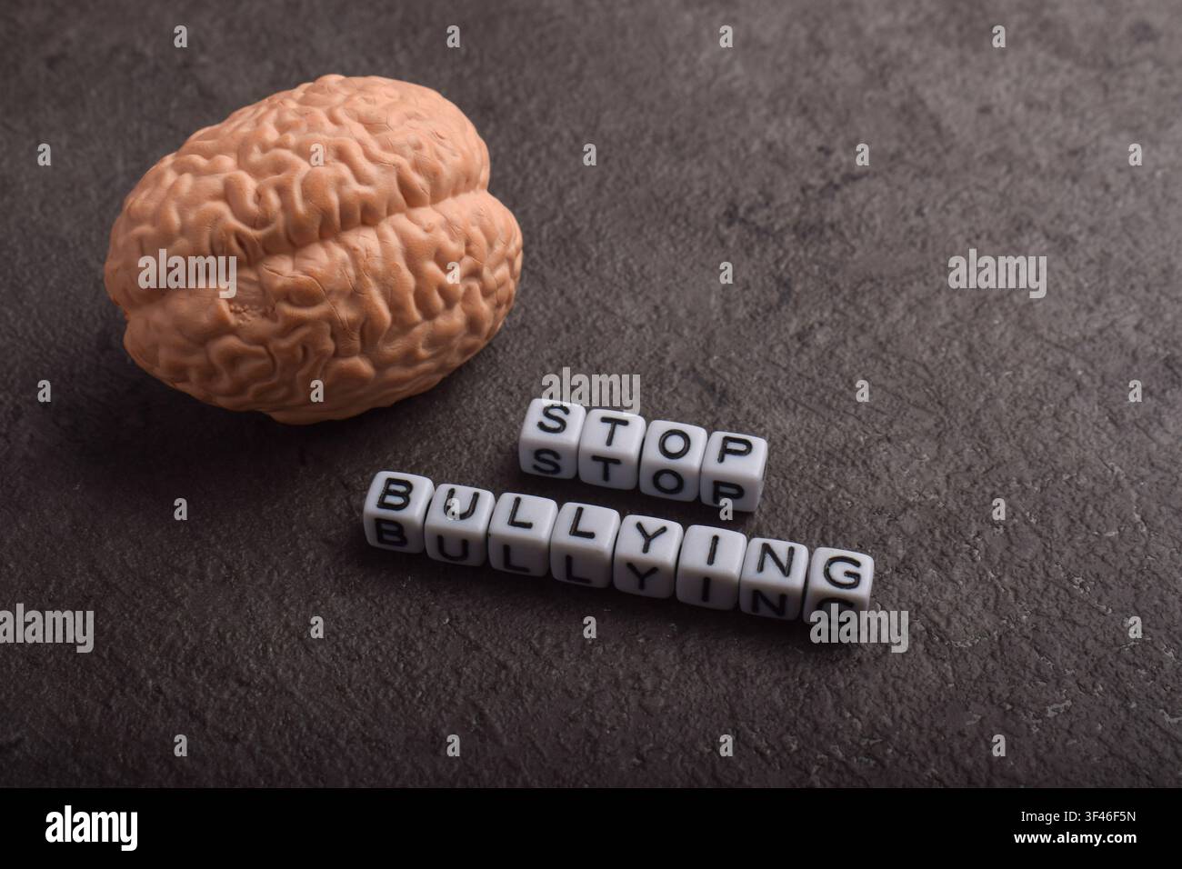 Modello di cervello accanto al testo "Stop al bullismo" su uno sfondo scuro textureggiato, rappresentante l'impatto sulla salute mentale, il danno psicologico e la campagna di sensibilizzazione Foto Stock