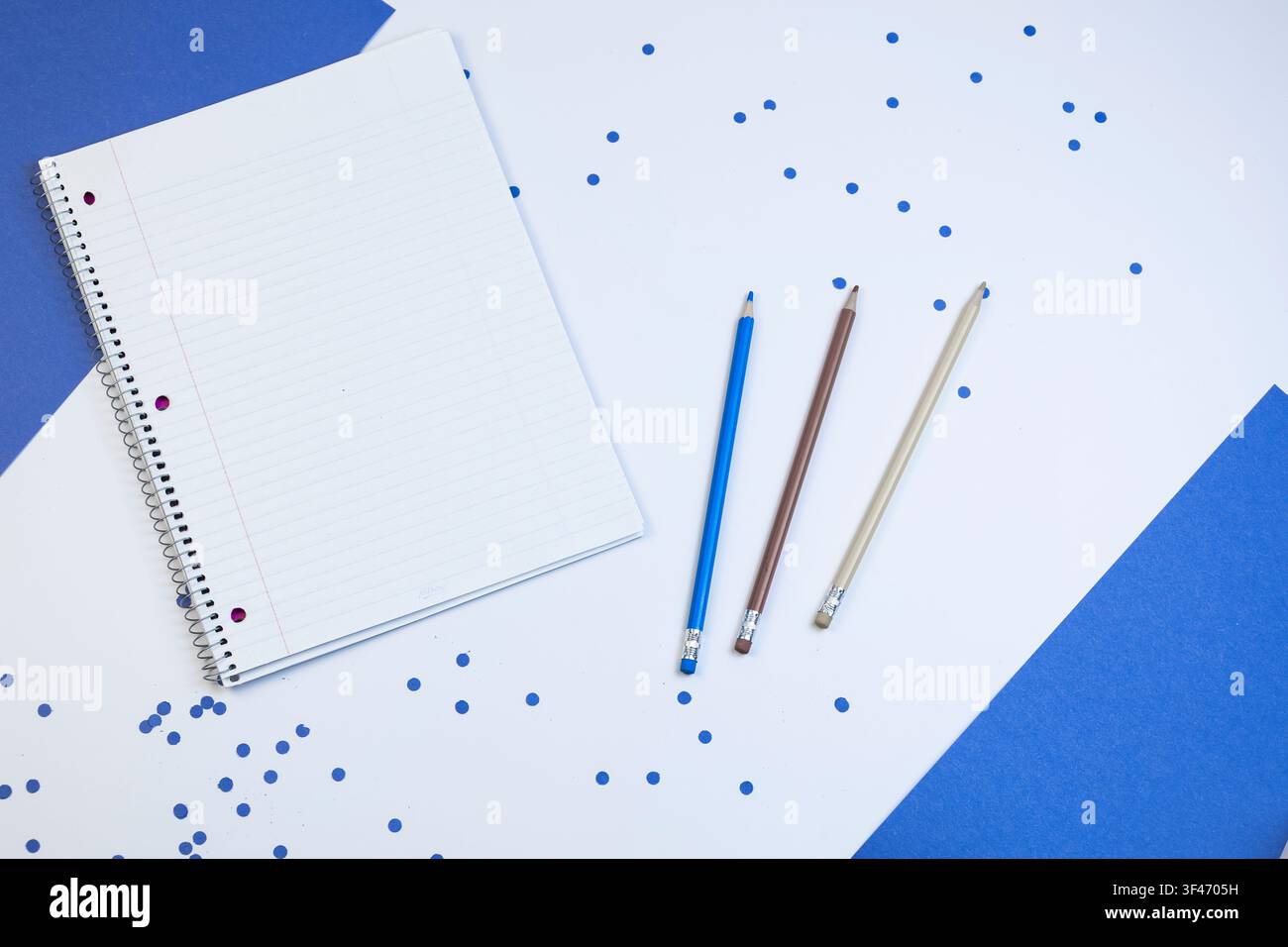 Quaderno e matite in flatlay con coriandoli blu su sfondo bianco e blu Foto Stock