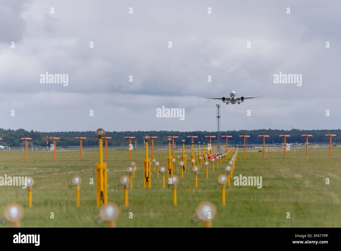 Riga, Lettonia - 21 luglio 2026: aereo passeggeri che si avvicina alle luci della pista di atterraggio per l'atterraggio all'aeroporto internazionale di Riga sotto un cielo estivo nuvoloso. Foto Stock