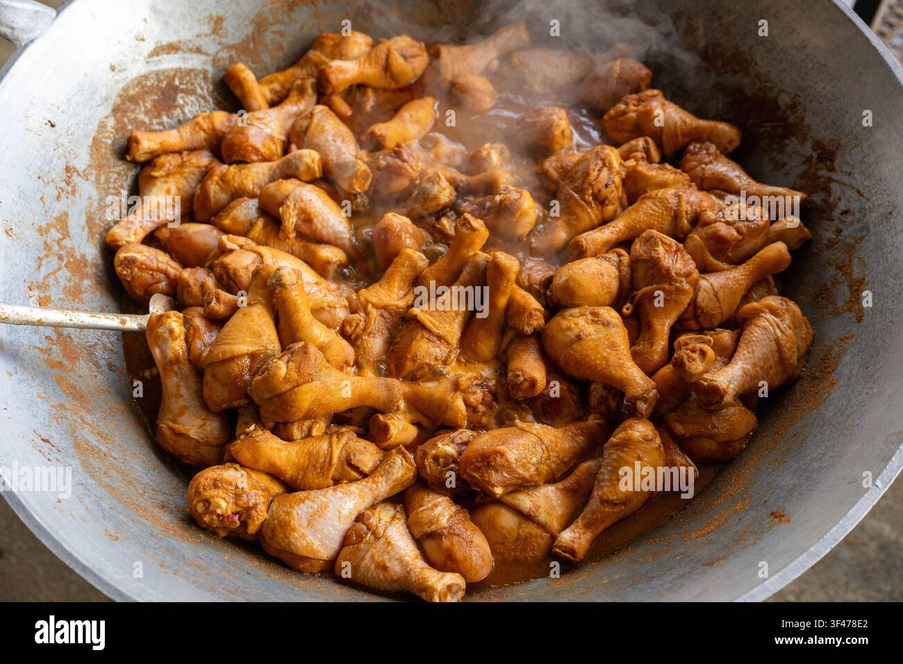 Un drumstick di pollo brasato e piccante in un grande wok di metallo, fumante e condito con una ricca salsa marrone, scena di street food appetitosa con un aroma saporito e sostanzioso Foto Stock