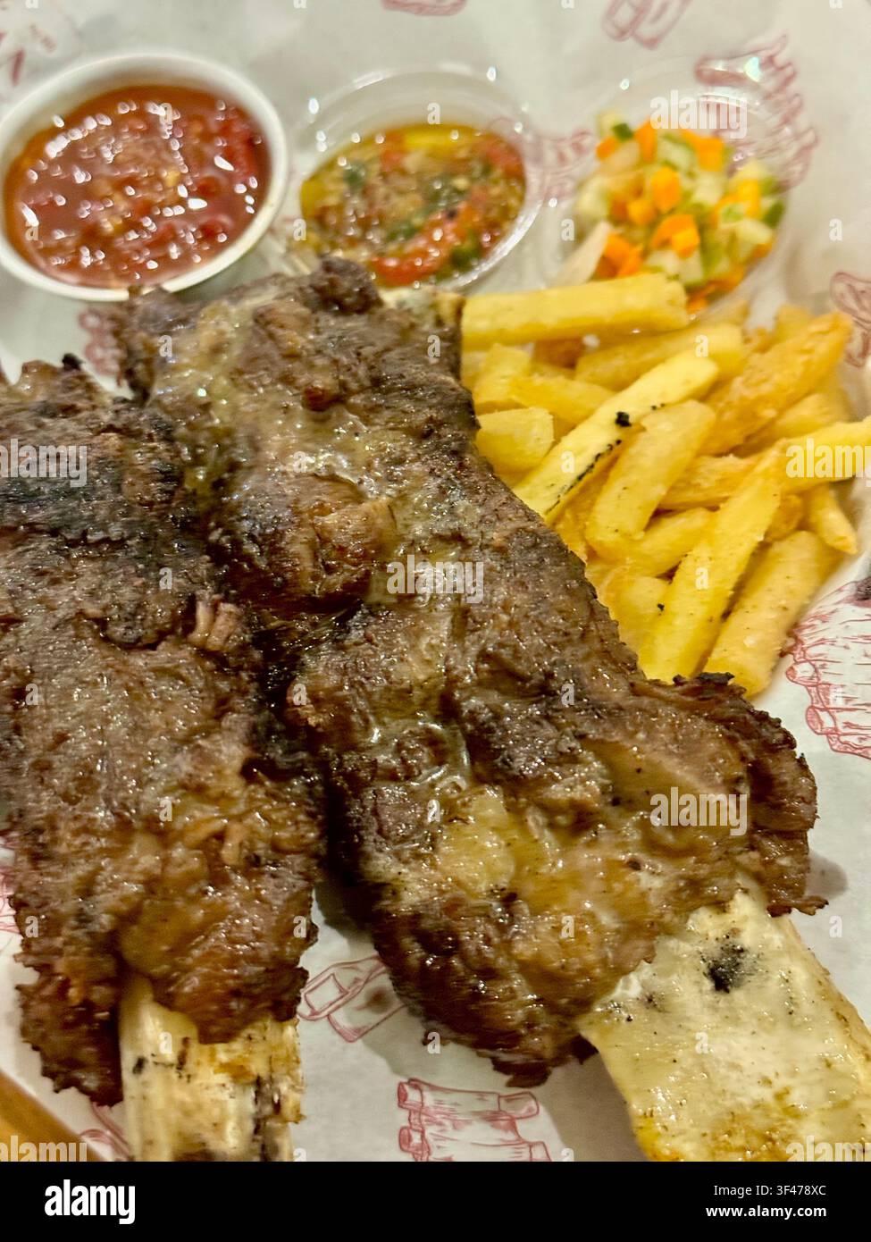 Costine di manzo fritte croccanti servite con patatine fritte, salse al chili e verdure su un piatto da ristorante. Foto Stock