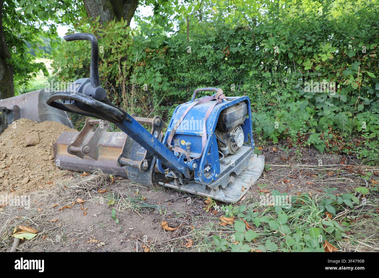 Compattatore a piastra vibrante blu in piedi accanto a un cantiere edile pronto per la compattazione del terreno. Foto Stock