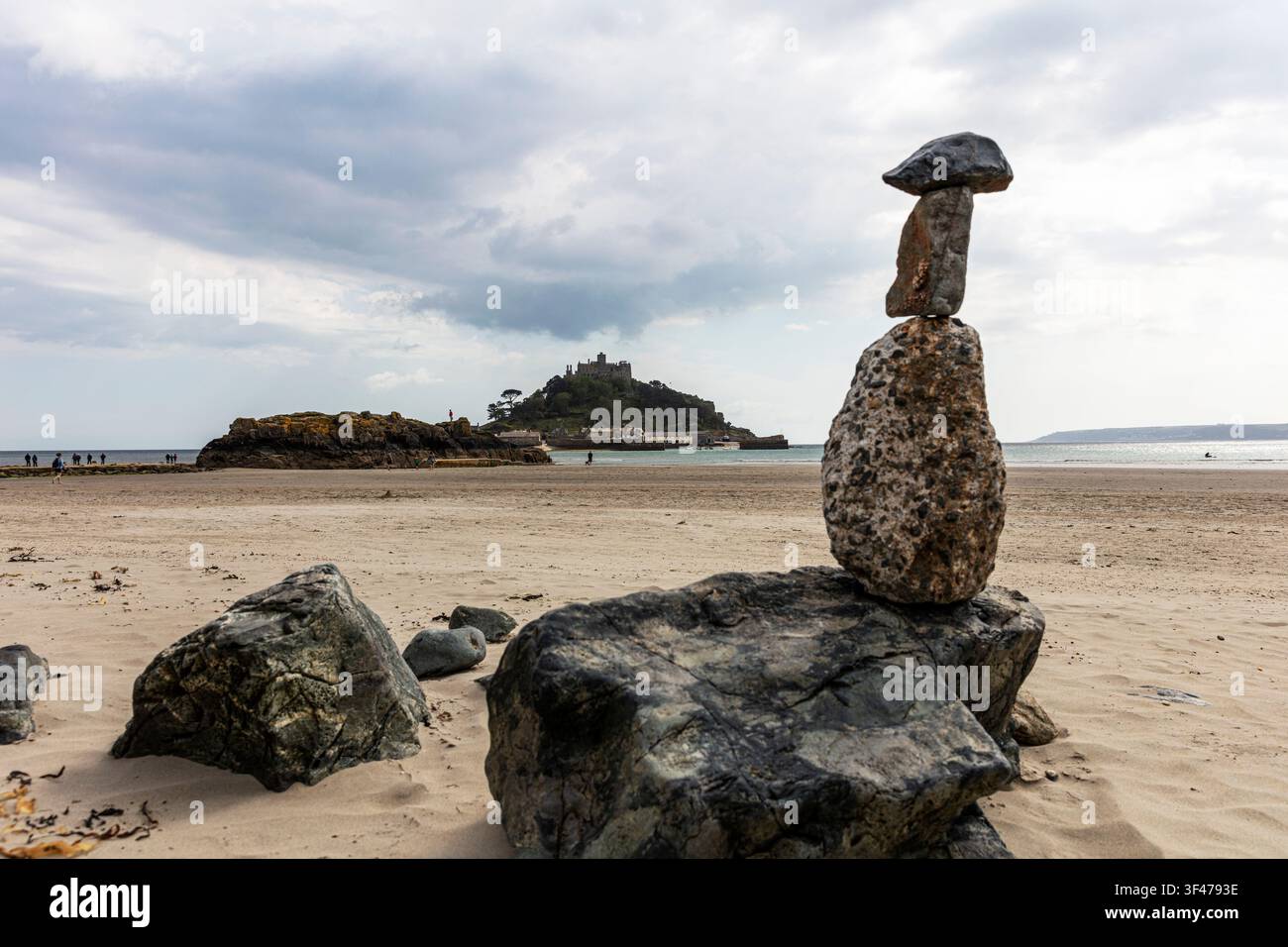 Monte San Michele in Cornovaglia, con una pila di pietre bilanciate posta su una roccia in primo piano. La spiaggia sabbiosa, rocce sparse e la riva a bassa marea Foto Stock