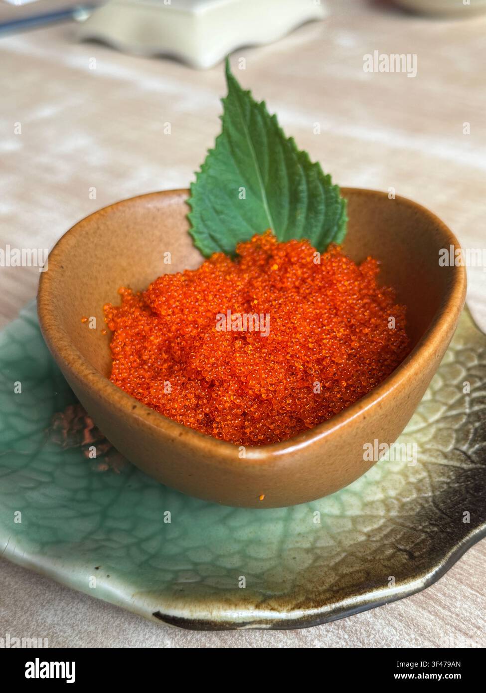 Roe di pesce volante Tobiko servito come antipasto di frutti di mare giapponesi, presentato in una ciotola decorativa con una guarnizione di foglia di shiso fresca. Foto Stock