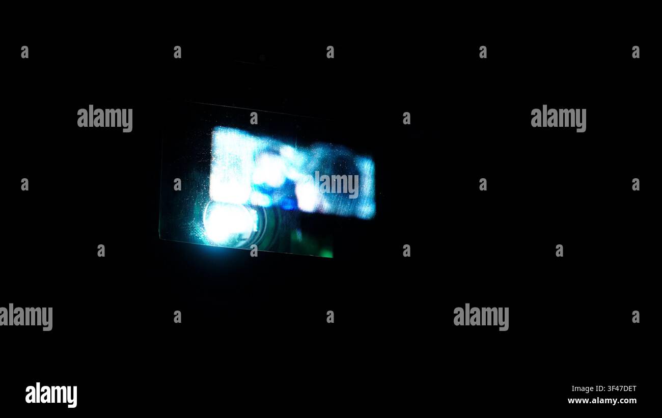 Lente del proiettore che brilla intensamente, proiettando un fascio di luce vivido con immagini astratte di film su una superficie in un ambiente buio, creando un'atmosfera cinematografica e Foto Stock