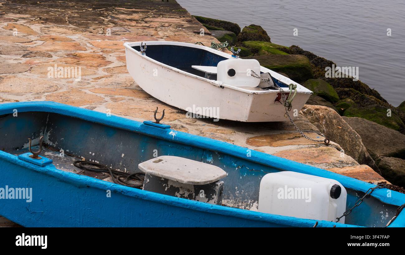Barche a remi in legno blu e bianche tirate su un molo di granito, Portogallo Foto Stock