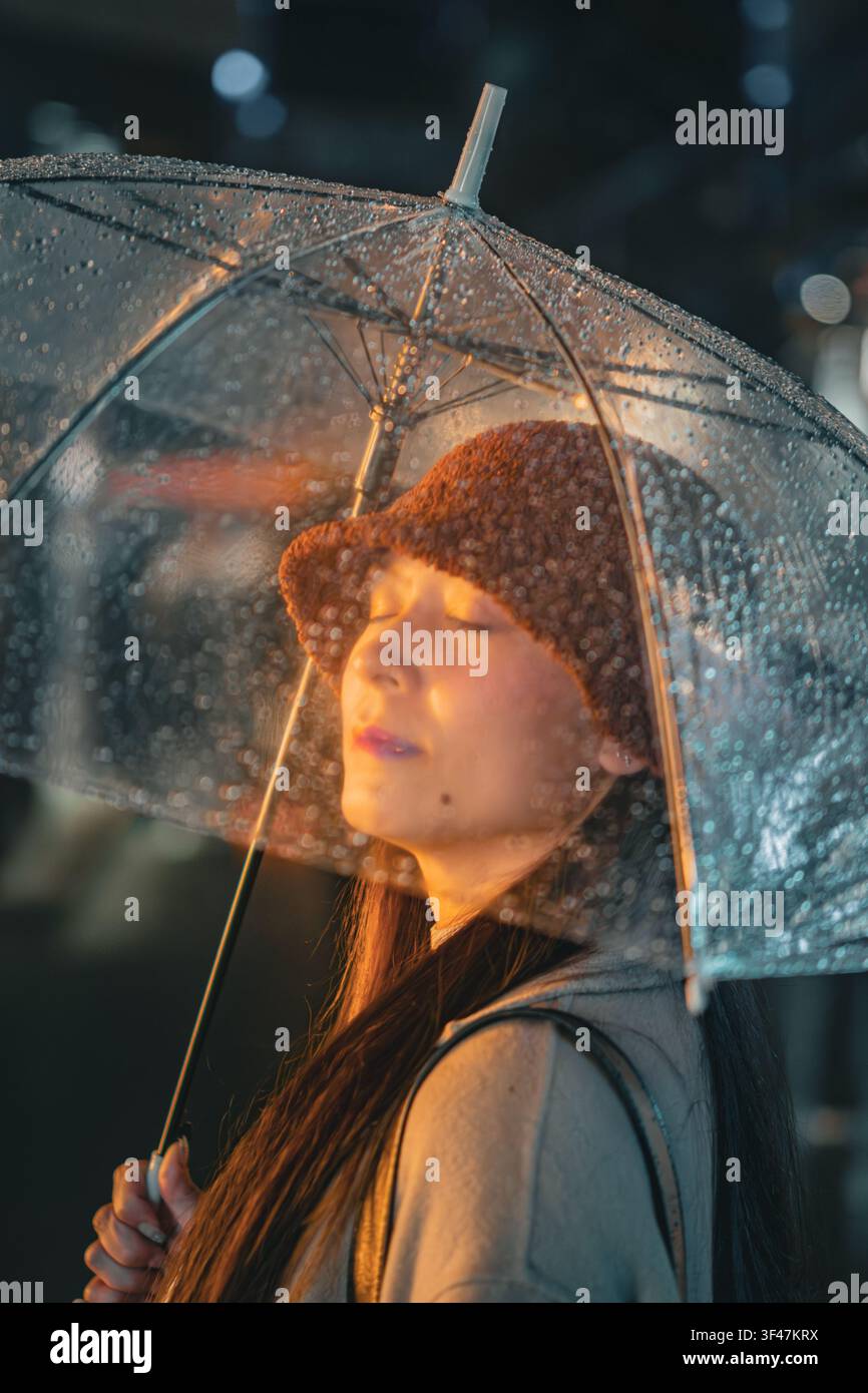 Donna con gli occhi chiusi che si rifugia sotto un ombrello luminoso, Shanghai, Cina Foto Stock
