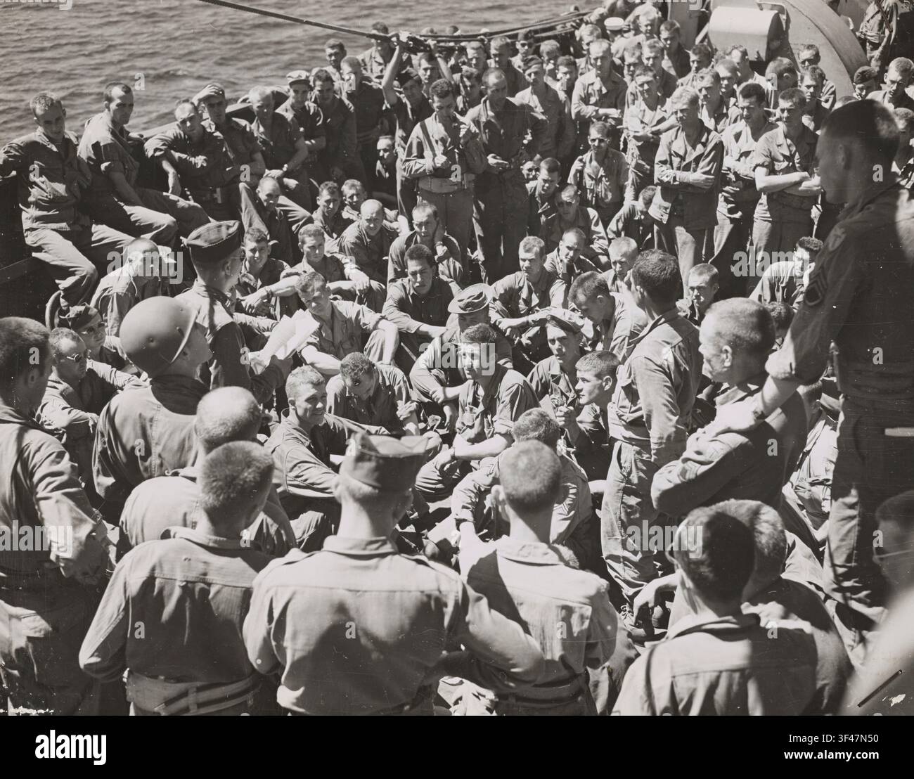Ufficiali e truppe statunitensi affollano il ponte di un trasporto da combattimento gestito dalla Guardia Costiera per discutere gli ultimi dettagli della loro missione mentre la nave naviga verso la terraferma italiana. Un ufficiale legge ad alta voce le istruzioni mentre i soldati si radunano stretti intorno a lui, alcuni seduti sulle ringhiere e sugli equipaggiamenti del ponte, altri in piedi spalla a spalla. I membri della Guardia Costiera che manovrano la nave da sbarco hanno ricevuto attente istruzioni sulla natura delle spiagge d'invasione, con l'intero attacco coordinato nei minimi dettagli da ufficiali dell'Esercito, della Marina e della Guardia Costiera che hanno lavorato insieme prima dell'assalto. Foto Stock