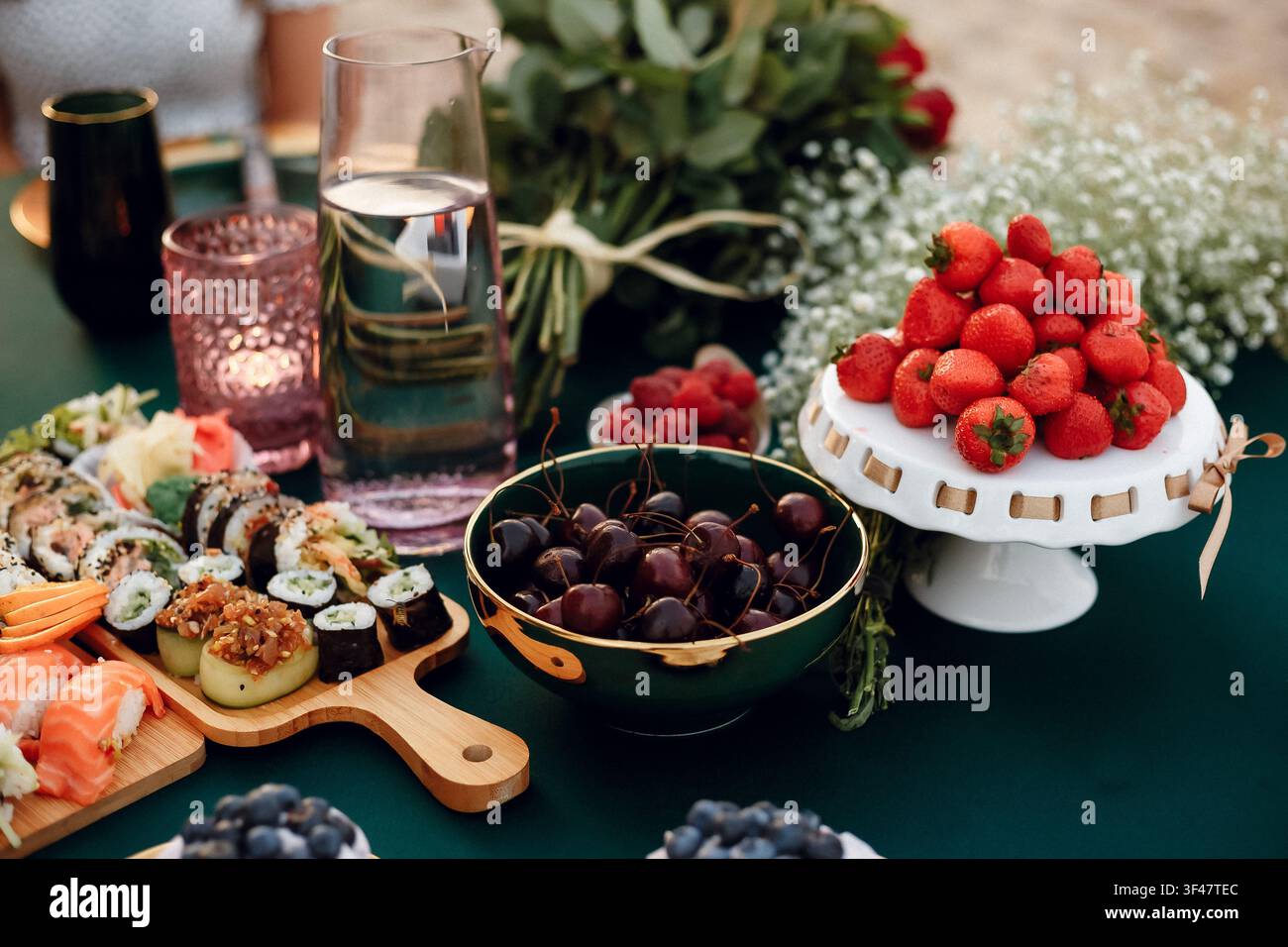 Elegante riunione all'aperto con sushi fresco, fragole e ciliegie su una tovaglia verde scuro. Catering per feste estive di lusso Foto Stock