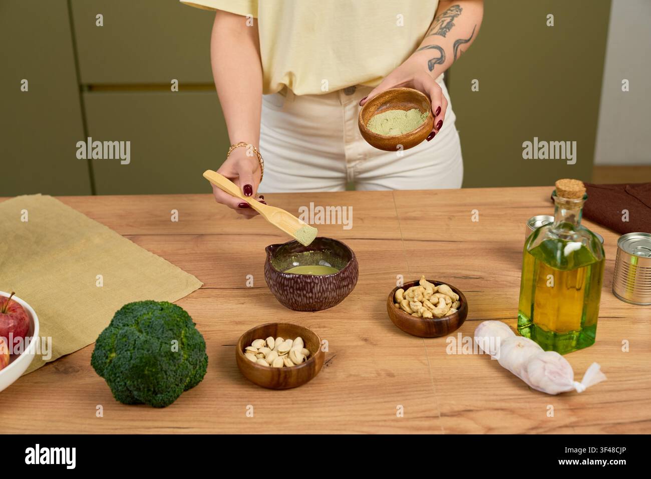 Una persona mescola della polvere di matcha in una ciotola, circondata da verdure fresche e noci per una bevanda vegana. Foto Stock
