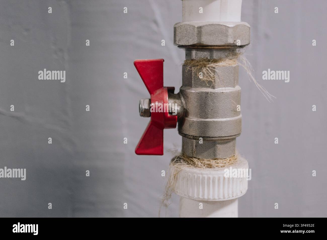 Valvola a sfera in metallo con maniglia a farfalla rossa installata su tubo di plastica bianco per idraulica all'interno Foto Stock