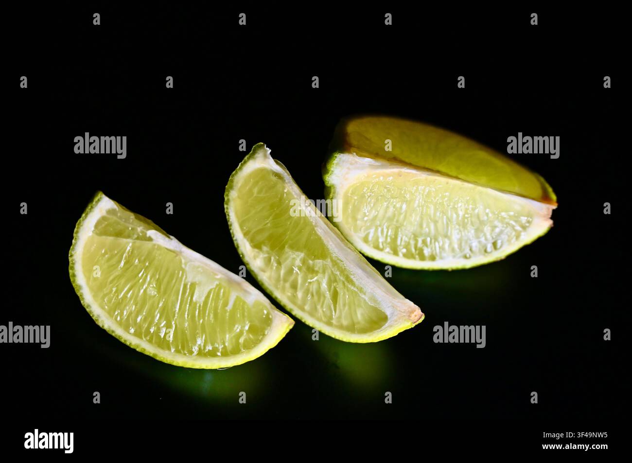 Una foto macro discreta di tre segmenti di limone vivaci allineati in diagonale su una superficie nera come la pece, evidenziando la trama della polpa, la lucentezza naturale e i toni verdi vivaci. Foto Stock
