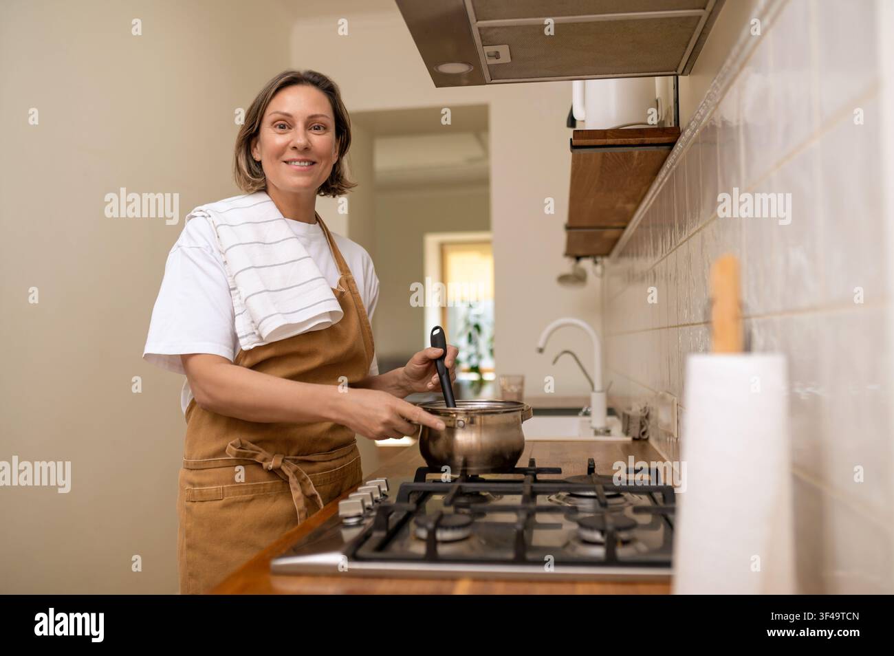 Donna sorridente di mezza età che mescola il cibo in una pentola Foto Stock