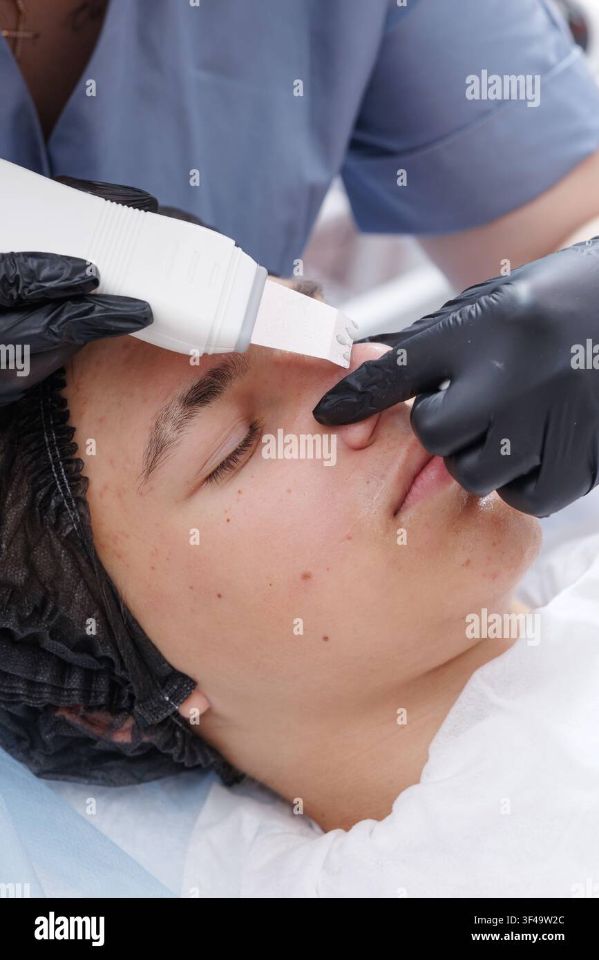 Una sessione professionale di pulizia del viso ad ultrasuoni utilizzando uno scrubber per rimuovere i punti neri e l’eccesso di sebo, promuovendo un incarnato più chiaro e una pelle più sana Foto Stock