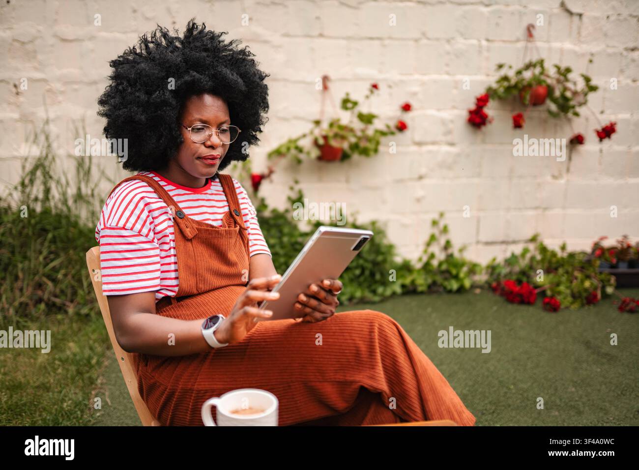 Donna nera che si rilassa nel cortile usando un tablet digitale Foto Stock