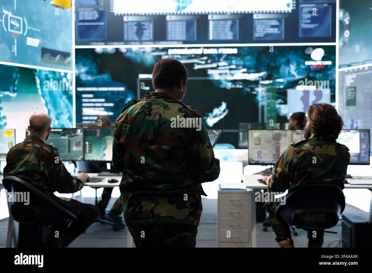 Squadra di ufficiali militari che monitora i display di sorveglianza nella sala operativa. I supervisori dell'esercito supervisionano gli operatori che tracciano mappe satellitari e informazioni sugli obiettivi Foto Stock
