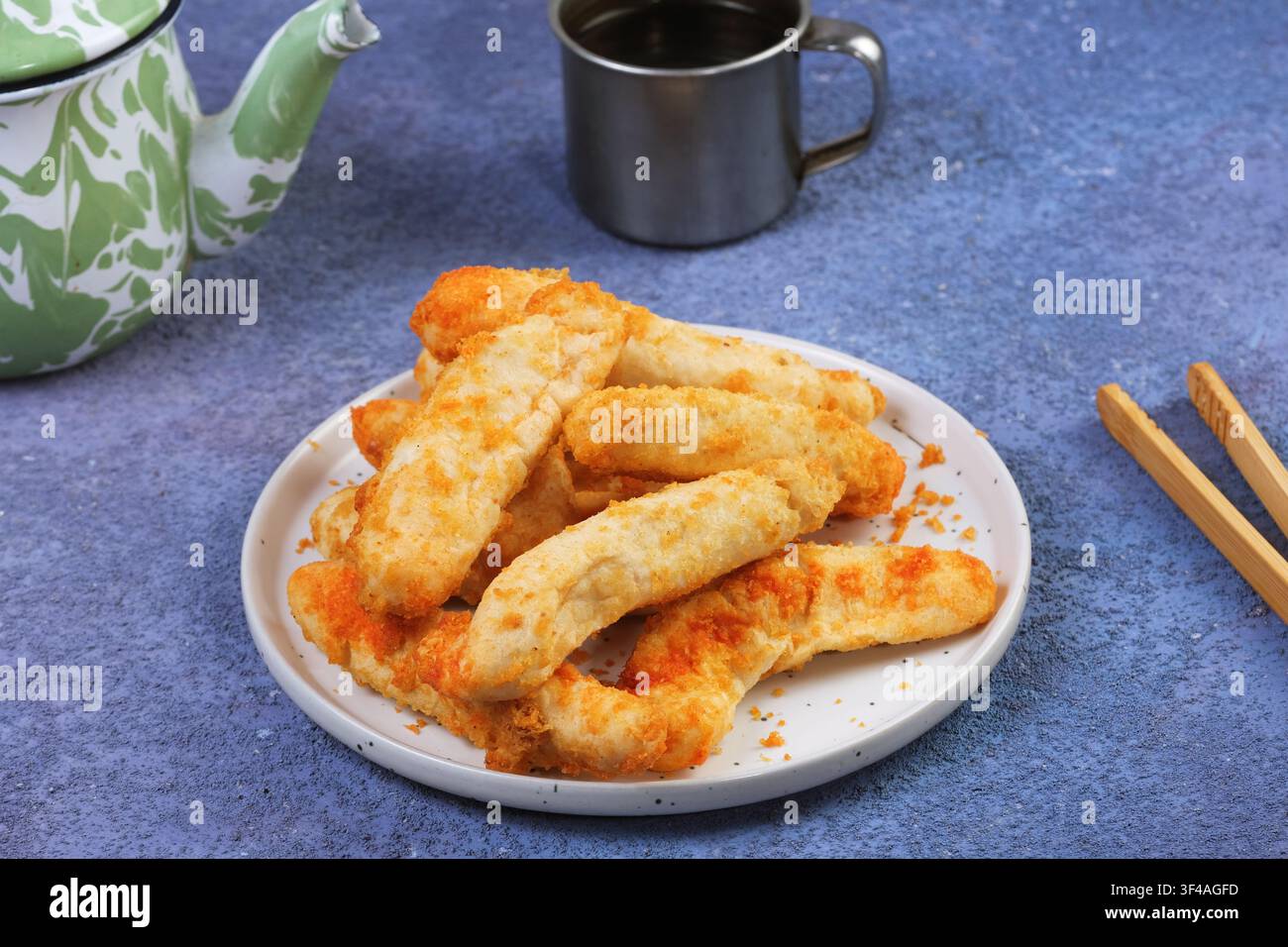 Croccanti polpette di pesce indonesiane otak otak disposte su un piatto bianco con bacchette e una teiera tradizionale sullo sfondo. Foto Stock