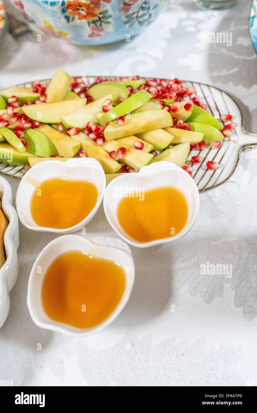 Mele verdi affettate e semi di melograno sono disposti su un vassoio. Piccole ciotole contengono miele. Questa disposizione fa parte delle tradizioni di Rosh Hashanah per accogliere il nuovo anno. Foto Stock