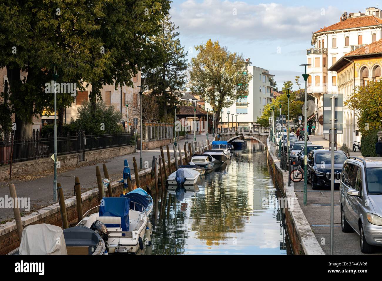 Lido di Venezia, Venezia, Italia - 25 ott. 2025: Il Canal Via Lepanto con barche ormeggiate e un ponte di pietra fiancheggiato da edifici Foto Stock