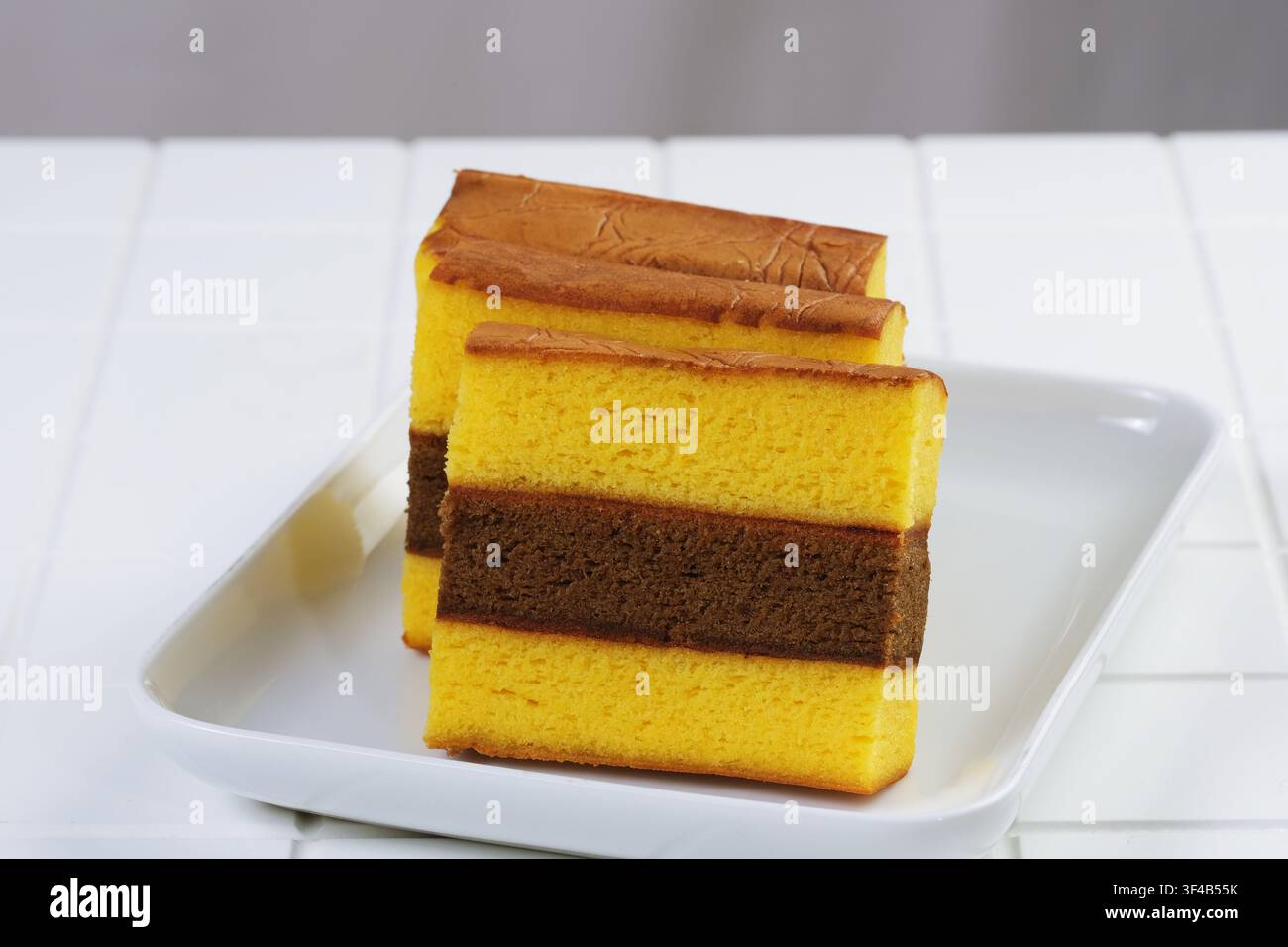 Tradizionale torta indonesiana spiku o kue lapis surabaya servita con tè su tavolo bianco, che rappresenta il concetto di comfort food, colazione e spuntino. Foto Stock