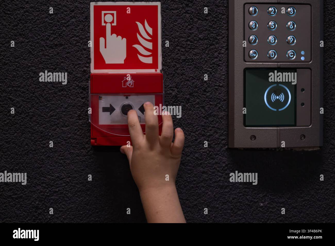 Bambino che preme il punto di chiamata manuale per l'allarme antincendio accanto a un moderno sistema di controllo degli accessi Foto Stock