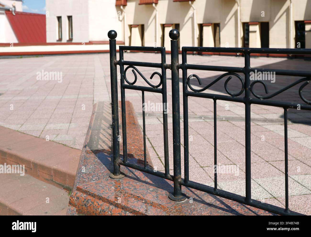Ringhiera in ferro battuto scalini in granito terrazza. Recinto decorativo vintage in metallo su gradino in granito rosso lucido con pavimentazione sfocata e edificio storico Foto Stock
