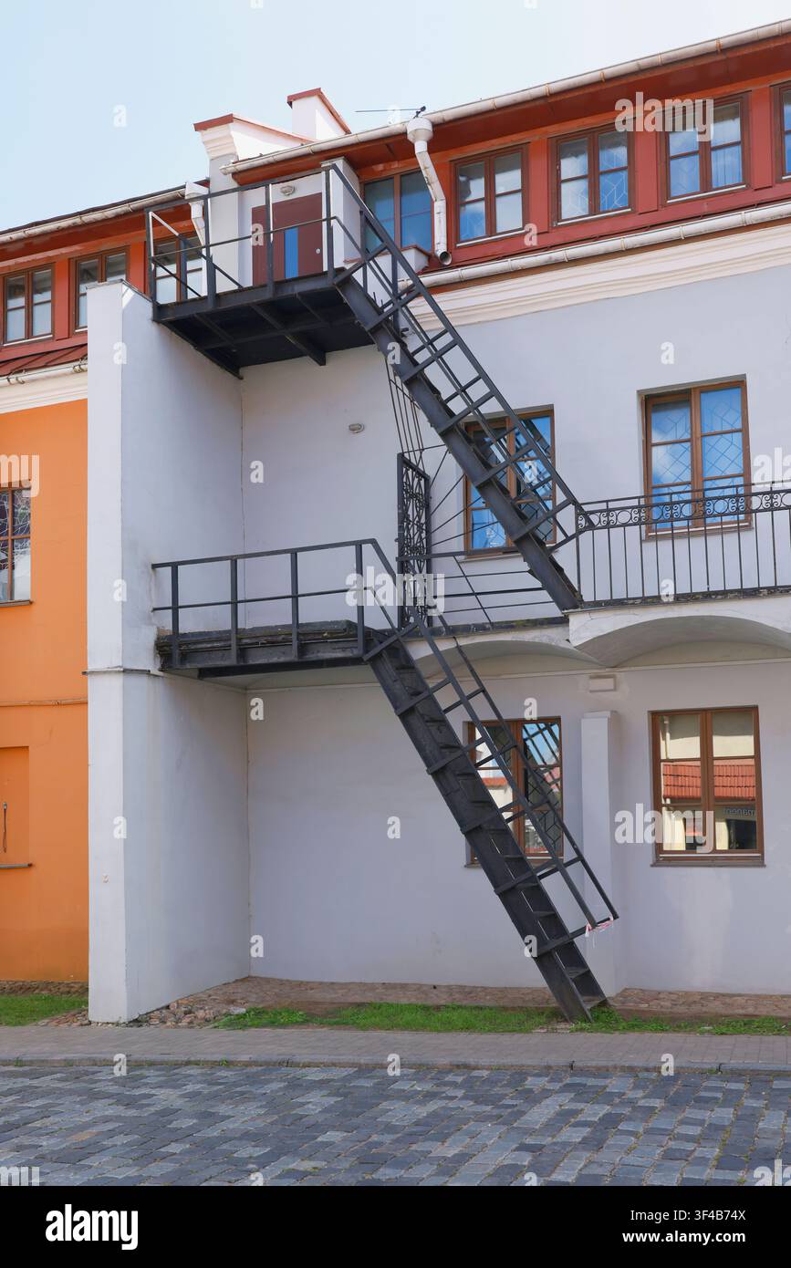 Scalinata antincendio industriale in metallo sulla facciata dell'edificio. Struttura di scala di emergenza esterna in ferro nero su muro architettonico di vecchia casa rinnovata Foto Stock
