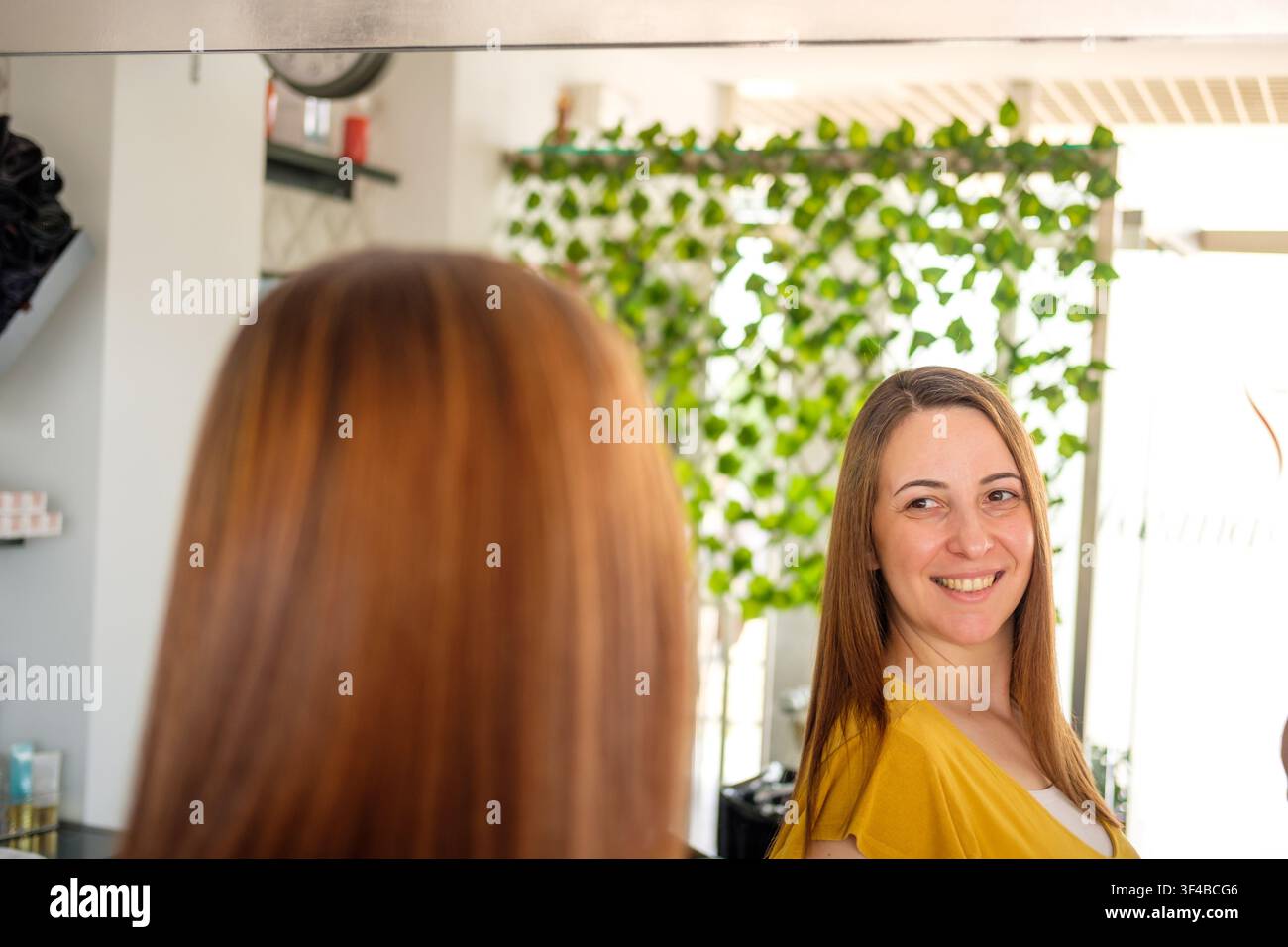 Donna che guarda soddisfatta la sua nuova acconciatura riflessa nello specchio del salone Foto Stock
